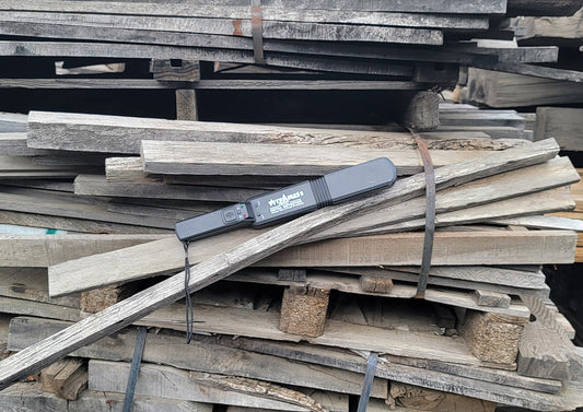 Lumber Wizard 5 woodworking metal detector resting on a stack of weathered pallet wood with metal banding