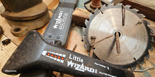 Lumber Wizard 5 and Little Wizard 2.5 metal detectors next to a damaged saw blade and rusty nails on a workshop bench