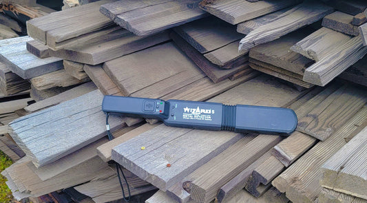 Lumber Wizard 5 metal detector resting on a stack of weathered reclaimed demolition lumber