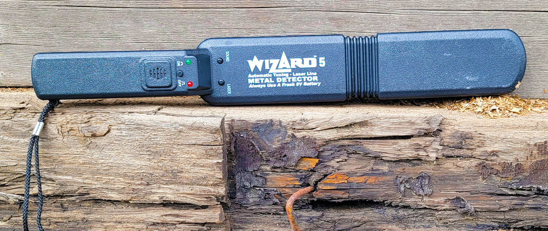 Wizard 5 metal detector resting on weathered barn wood beam with a rusty nail visible underneath